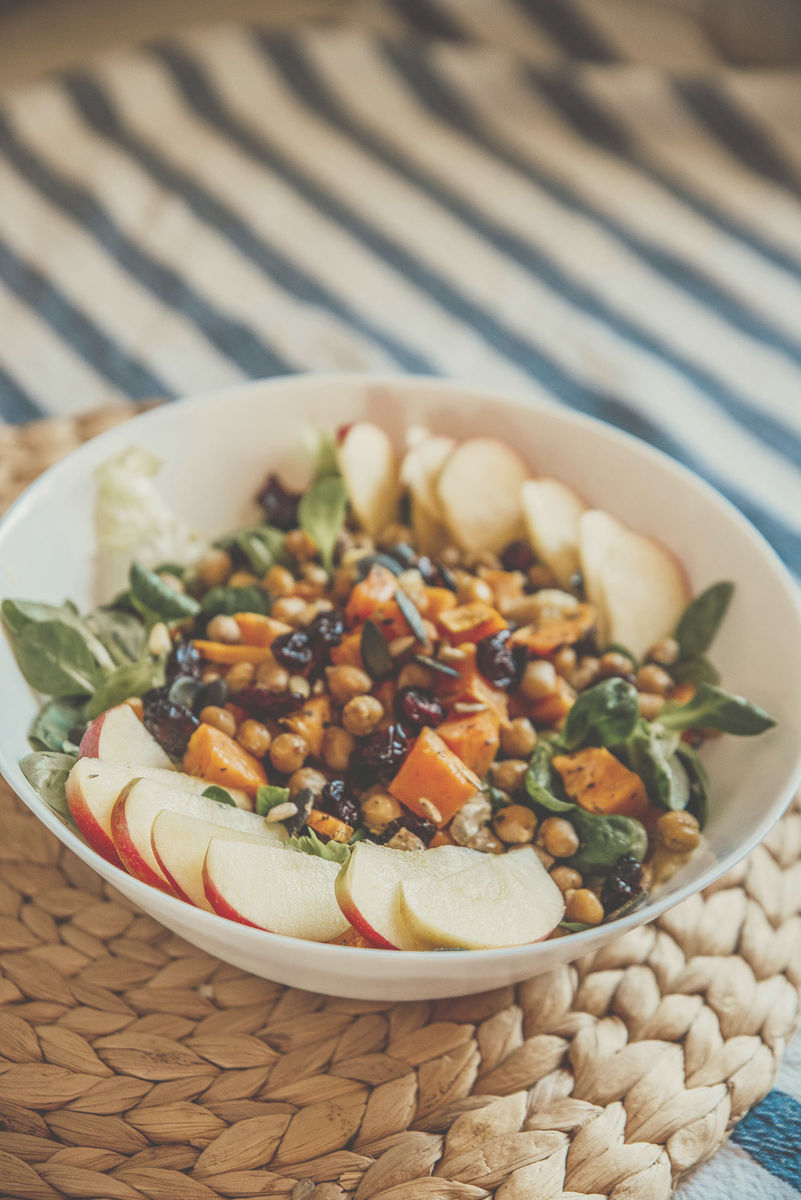 Bol coloré de salade anti-inflammatoire composée de pois chiches rôtis, dés de patate douce, cranberries séchées, jeunes pousses de salade et tranches de pomme fraîche.