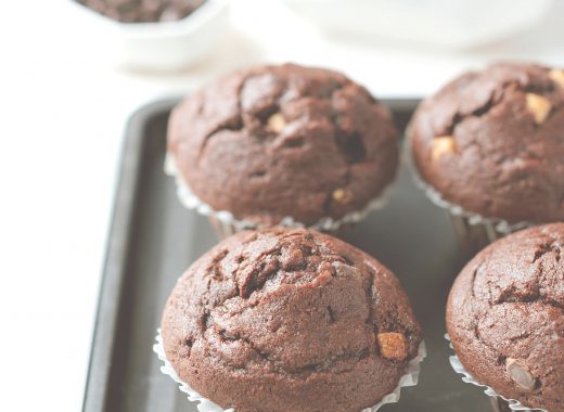 Quatre muffins au chocolat moelleux disposés sur une plaque de cuisson, avec en arrière-plan des morceaux et copeaux de chocolat.