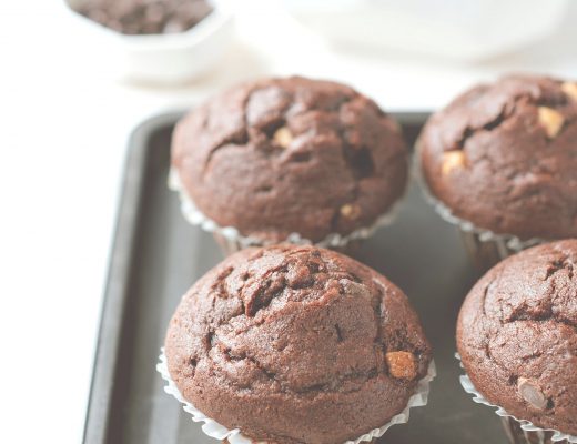 Quatre muffins au chocolat moelleux disposés sur une plaque de cuisson, avec en arrière-plan des morceaux et copeaux de chocolat.